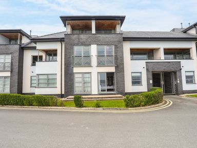 A multi-story residential building with balconies and ground floor windows with hedges in front at Four The Quay in Red Wharf Bay