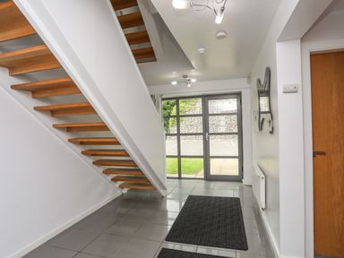 A hallway with floating wooden stairs glass door mats and a wall mirror at Four The Quay in Red Wharf Bay