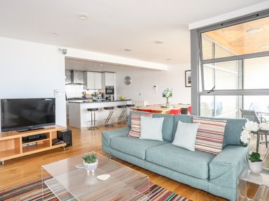 An open living space with a blue sofa beside a glass coffee table and a television on a wooden stand at Four The Quay in Red Wharf Bay