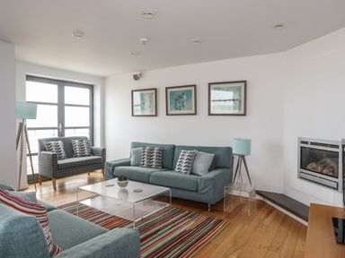 A living room with two teal sofas a patterned armchair a glass coffee table and a fireplace at Four The Quay in Red Wharf Bay