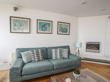 A sitting room with a teal sofa cushions and framed bird pictures above at Four The Quay in Red Wharf Bay