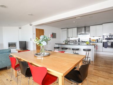 A kitchen and dining area with a wooden table and red and black chairs at Four The Quay in Red Wharf Bay