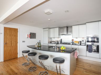 A kitchen with a black countertop island with four stools and various appliances at Four The Quay in Red Wharf Bay