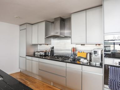 A kitchen with cabinets a gas stove a toaster a knife block a kettle a coffee machine and a cutting board at Four The Quay in Red Wharf Bay