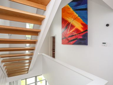 A staircase with wooden steps and a colorful abstract painting on a white wall at Four The Quay in Red Wharf Bay