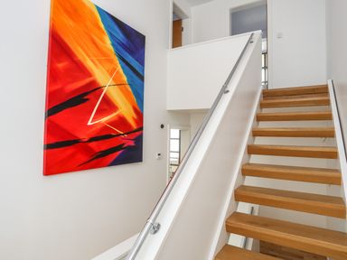 A staircase with wooden steps and a metal handrail with abstract colorful painting on the wall at Four The Quay in Red Wharf Bay