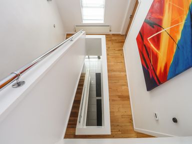A hallway with wooden floor and a staircase leading down featuring a metal handrail and colorful abstract painting on the wall at Four The Quay in Red Wharf Bay