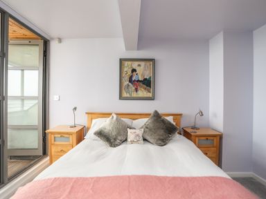 A bedroom with a wooden bed framed by two wooden nightstands and a painting above the bed at Four The Quay in Red Wharf Bay