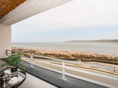 A balcony with a small table plant and teapot overlooking a beach and sea at Four The Quay in Red Wharf Bay