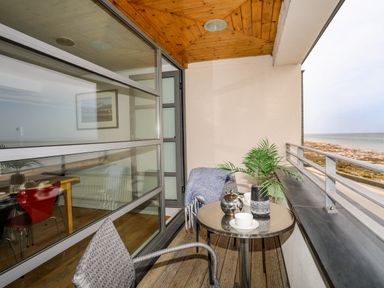 A balcony with two chairs a round table with cups a plant and a kettle overlooking the beach at Four The Quay in Red Wharf Bay
