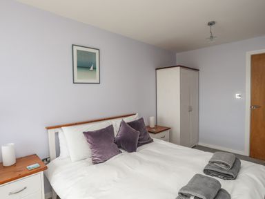 A bedroom with a bed with purple pillows two bedside tables with lamps a wardrobe and a door at Four The Quay in Red Wharf Bay
