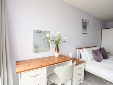 A bedroom with a desk chair bed with pillows and a vase with flowers at Four The Quay in Red Wharf Bay