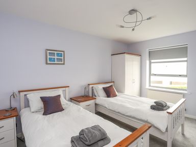 A bedroom with two single beds bedside tables lamps and a wardrobe at Four The Quay in Red Wharf Bay