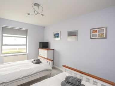 A bedroom with two beds a chest of drawers and a TV on a chest of drawers at Four The Quay in Red Wharf Bay