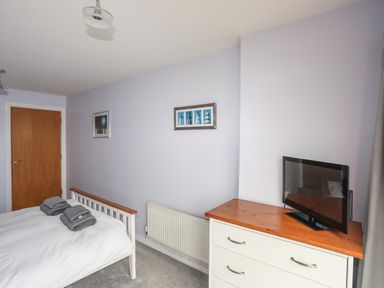 A bedroom with a bed with folded towels a wooden door a chest of drawers with a TV and framed pictures on the wall at Four The Quay in Red Wharf Bay