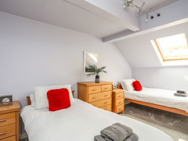 A bedroom with two single beds white bedding red pillows wooden furniture and a skylight window at Four The Quay in Red Wharf Bay