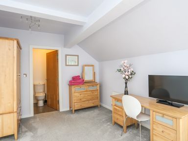 A bedroom with wooden furniture including a wardrobe dresser and desk a white chair a television and an open door leading to a bathroom at Four The Quay in Red Wharf Bay