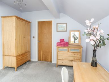 A room with wooden wardrobe wooden dresser with mirror and pink towels wooden table with vase and flowers at Four The Quay in Red Wharf Bay