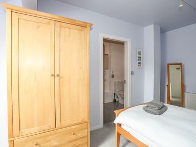 A bedroom with a wooden wardrobe a bed with towels a door leading to a bathroom and a standing mirror at Four The Quay in Red Wharf Bay