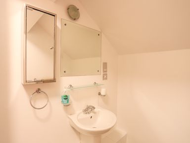 A bathroom sink with a mirror cabinet towel ring and soap dispenser at Four The Quay in Red Wharf Bay