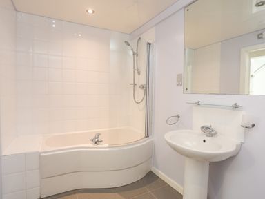 A bathroom with a bathtub and shower head next to a sink with a mirror above at Four The Quay in Red Wharf Bay