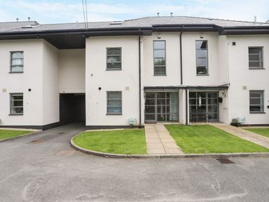 The front exterior of a modern two-story white building with multiple windows and grass patches at Four The Quay in Red Wharf Bay