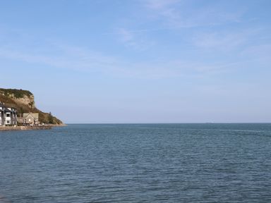 A coastal scene with houses on the left and a cliff next to the sea at Four The Quay in Red Wharf Bay