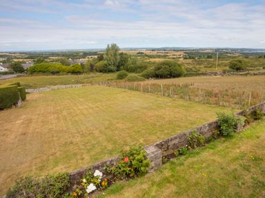 A fenced lawn area with flowers along a low stone wall and rural fields in the background at Frondeg in Rhiwlas