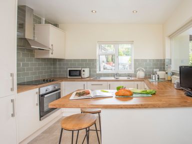 A kitchen with wooden countertops, built-in oven, microwave, sink, kettle, and stools at Frondeg in Rhiwlas