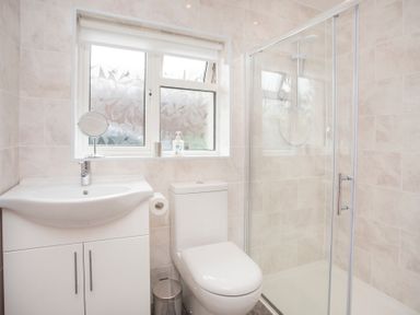 A bathroom with a sink, toilet, shower enclosure, and a window at Frondeg in Rhiwlas