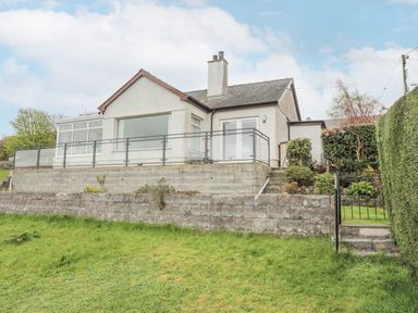 A house with a glass railing and concrete retaining walls surrounded by a grassy lawn at Frondeg in Rhiwlas