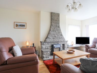 A living room with leather armchairs a stone fireplace wooden coffee table and a television at Frondeg in Rhiwlas