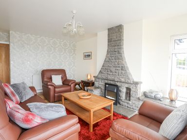 A living room with leather sofas a wooden coffee table and a stone fireplace at Frondeg in Rhiwlas