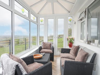 A sunroom with wicker chairs and sofa with cushions and a table with bowl and candles at Frondeg in Rhiwlas