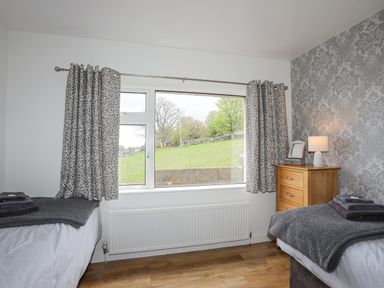 A bedroom with two single beds grey patterned curtains and a wooden chest of drawers at Frondeg in Rhiwlas