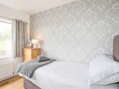 A bedroom with a single bed bedside table lamp and a window with patterned curtains at Frondeg in Rhiwlas