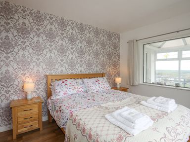 A bedroom with a double bed floral bedding wooden bedside tables lamps and a window overlooking a landscape at Frondeg in Rhiwlas