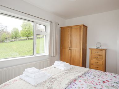 A bedroom with a bed covered with floral and patterned bedding two sets of folded towels on the bed a wooden wardrobe and chest of drawers in the corner with a small mirror on top at Frondeg in Rhiwlas