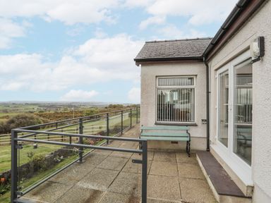 A patio with a bench and glass railing overlooking fields at Frondeg in Rhiwlas