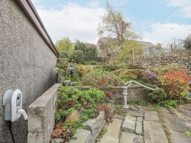 An outdoor garden area with stone steps plants bushes a water pump and a wall at Frondeg in Rhiwlas