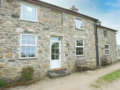 Stone house exterior with white windows wooden benches and a white door at Fron Fawr in Nefyn