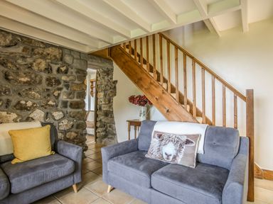A living room with two gray sofas under wooden stairs and a stone wall at Fron Fawr in Nefyn