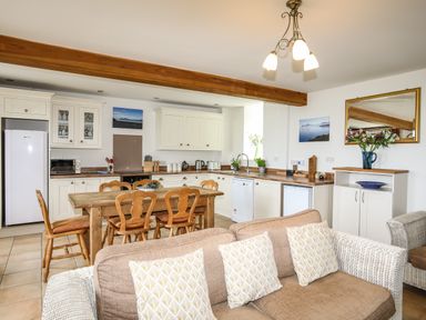 An open kitchen and dining area with wooden chairs around a table and a sofa with patterned cushions at Fron Fawr in Nefyn