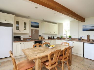 A kitchen with wooden table and chairs and white cabinets at Fron Fawr in Nefyn
