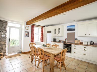 A kitchen with a wooden dining table and chairs white cabinets and tiled floor at Fron Fawr in Nefyn