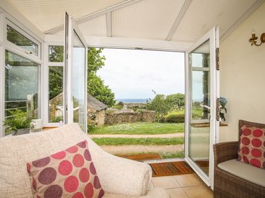 A conservatory with a beige armchair and patterned cushions overlooking a garden with a view of the sea at Fron Fawr in Nefyn