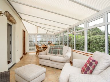 A conservatory with beige sofas a chair and an ottoman and a dining table with chairs at Fron Fawr in Nefyn