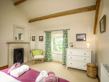 A bedroom with a bed, a wicker chair, a white dresser, and floral curtains at Fron Fawr in Nefyn