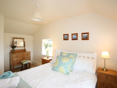 A bedroom with a bed two bedside tables lamps a wooden dresser with a mirror and three framed pictures on the wall at Fron Fawr in Nefyn