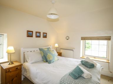 A bedroom with a double bed with blue and green pillows bedside tables with lamps and a window at Fron Fawr in Nefyn